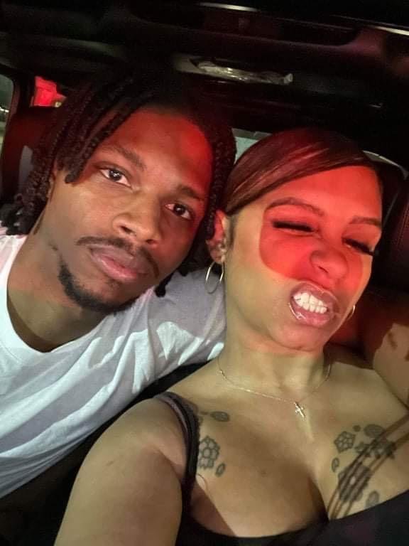 A man and a woman taking a selfie inside a vehicle, with the woman making a playful face and the man looking at the camera.