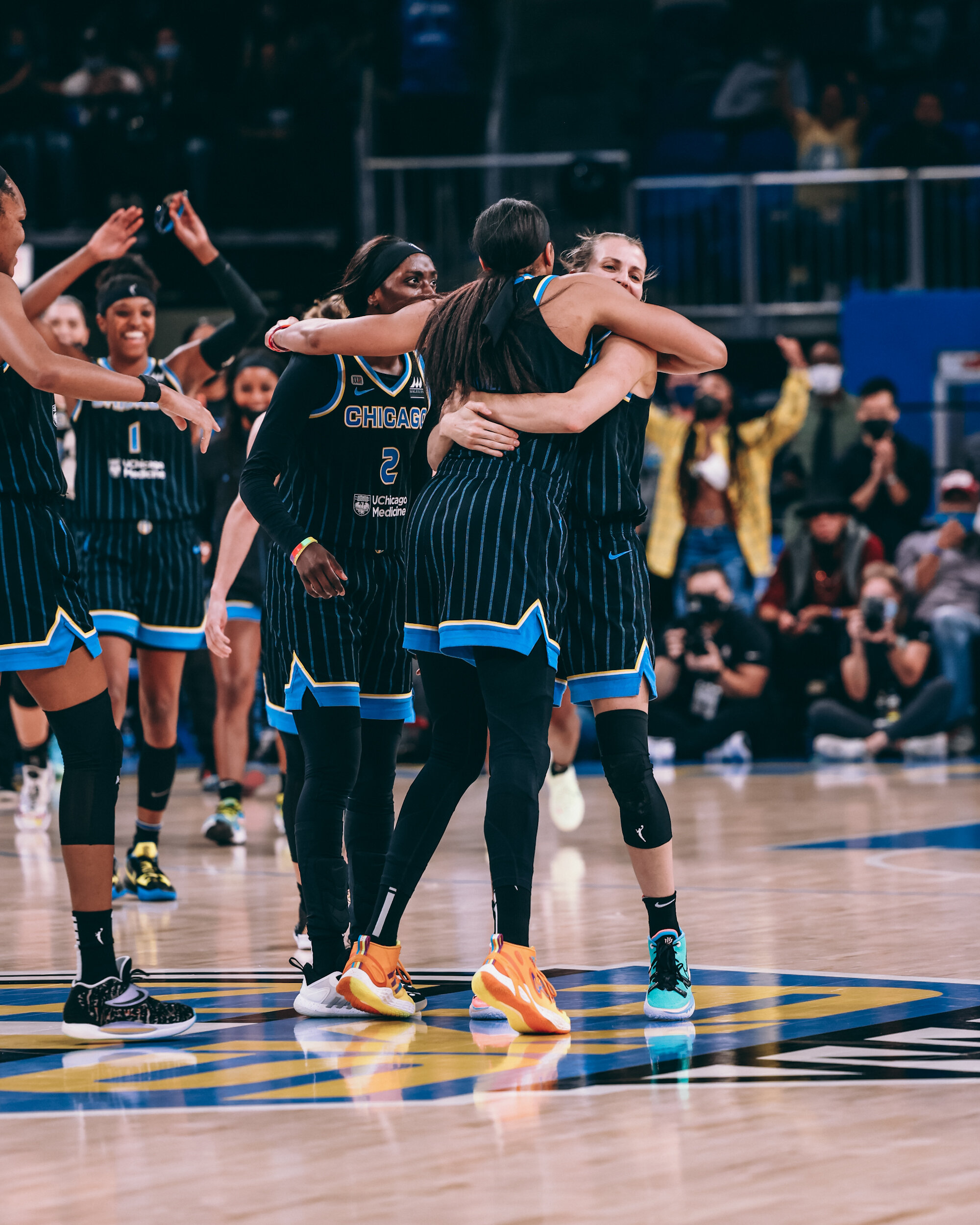 Women basketball players celebrating on the court during a game, some hugging and others smiling, wearing black and blue uniforms with 'Chicago' written on them.