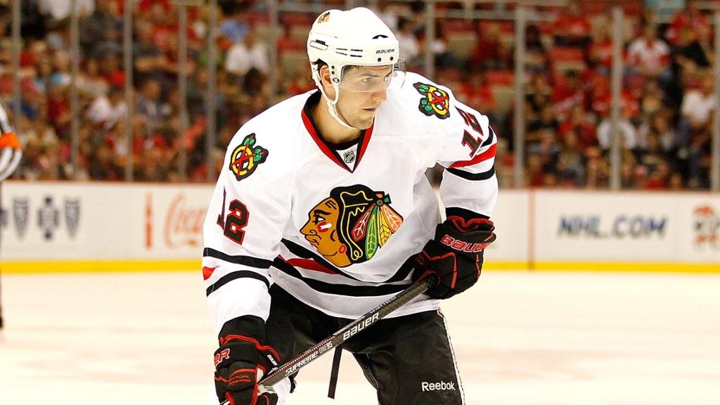 A hockey player wearing a white Chicago Blackhawks jersey and helmet on the ice during a game.