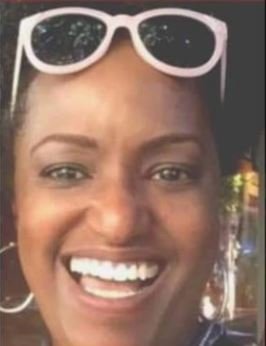 Close-up of a woman with dark skin smiling, wearing white sunglasses pushed up on her forehead.