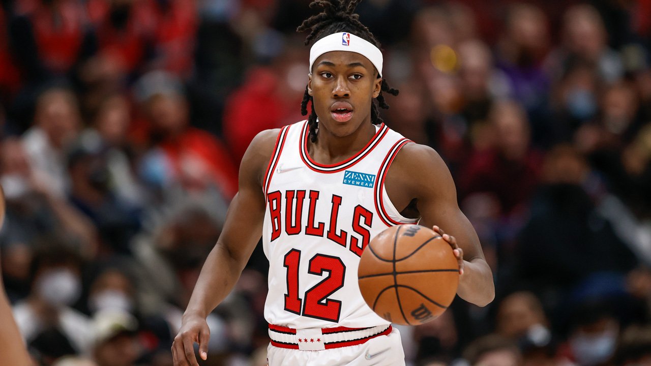 A basketball player from the Chicago Bulls wearing jersey number 12 with a white headband, holding a basketball on the court during a game.