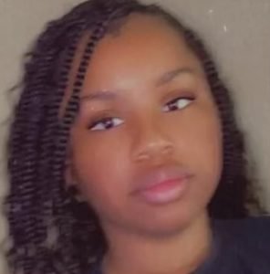 Close-up of a young woman with braided hair and a neutral expression.