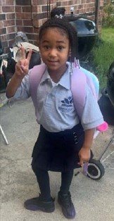 Young girl in school uniform holding a peace sign outdoors