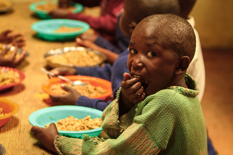 Children sitting at a long wooden table eating food from colorful plates.