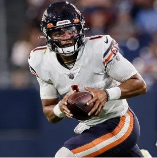An American football player in a white uniform with black helmet holding a football.