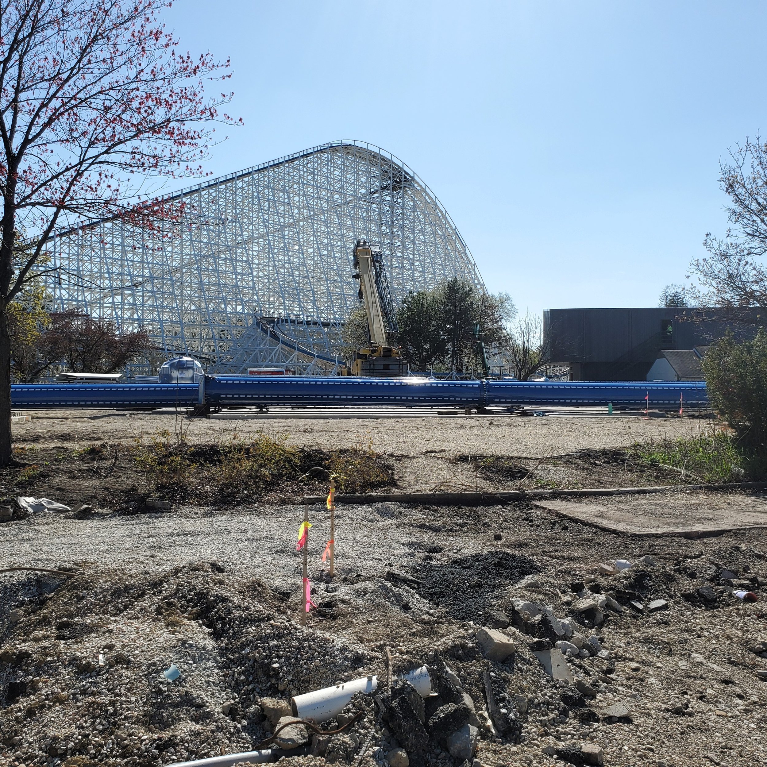Construction site with underground pipes and a roller coaster in the background in the distance.