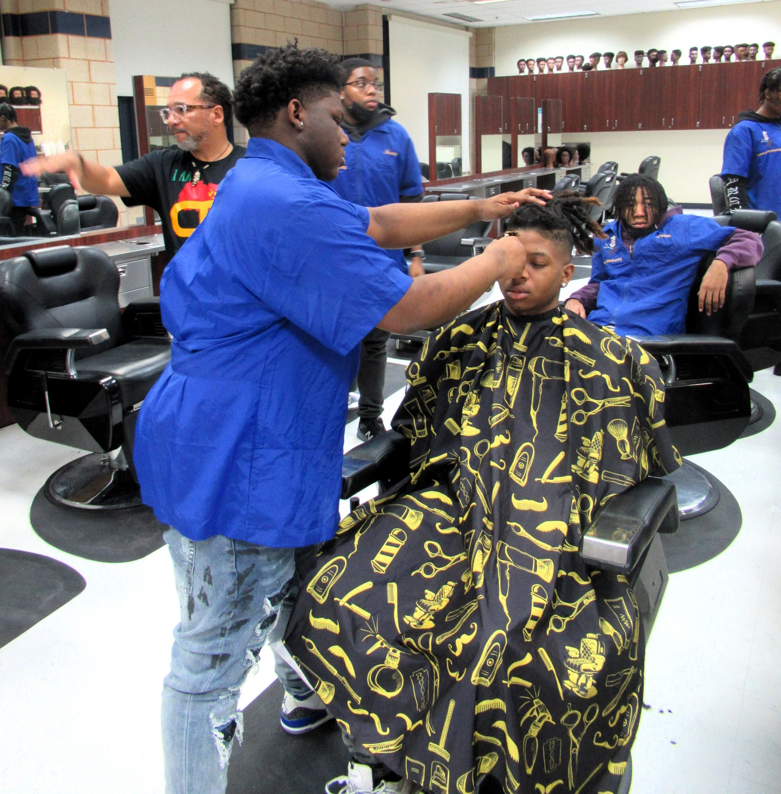 Barbershop scene with a man giving a haircut to a young man, while others wait or get haircuts in a barbershop.