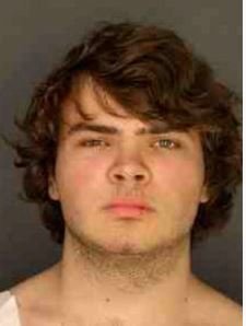 A young man with medium-length, wavy brown hair and a serious expression on his face.