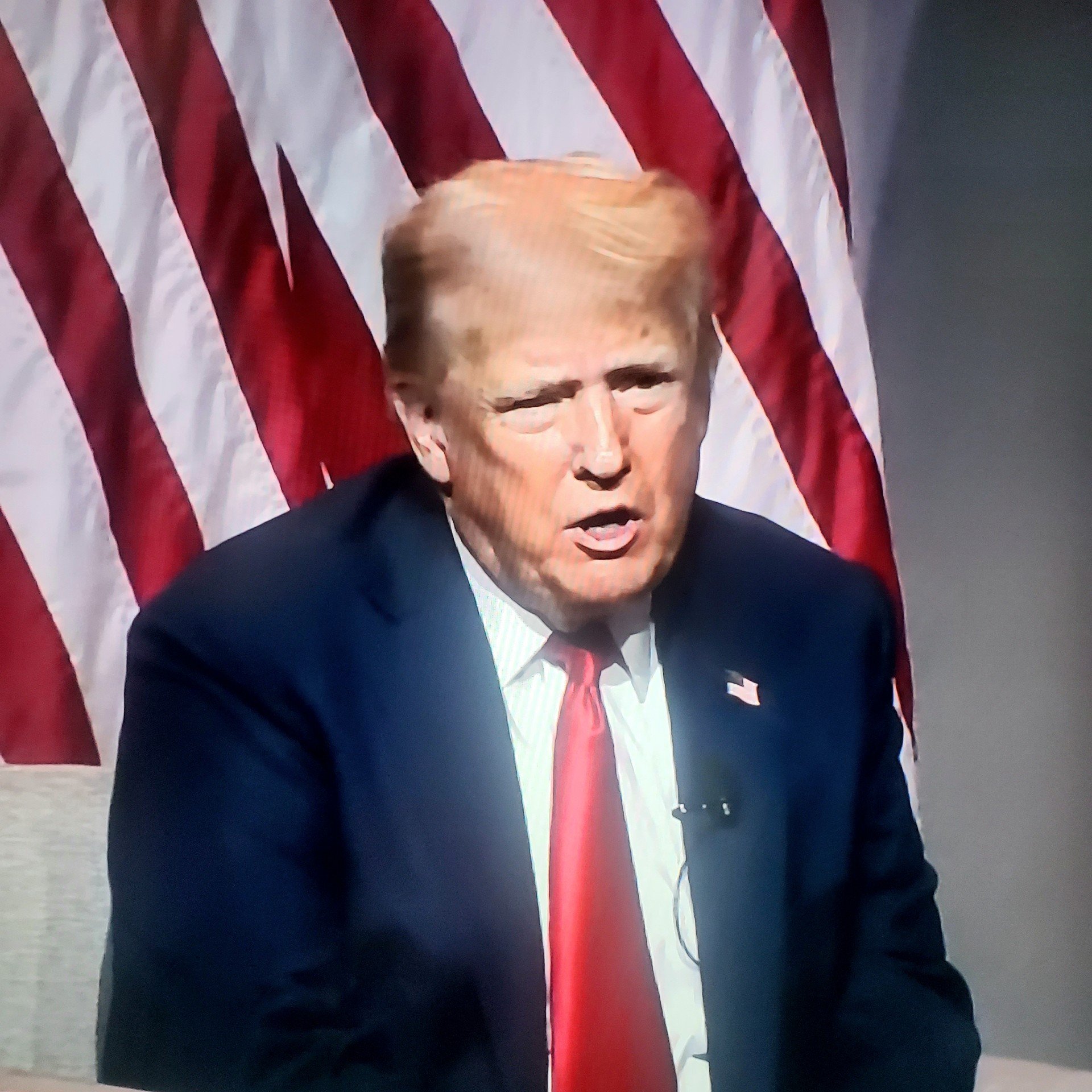 Former US President Donald Trump speaking with an American flag in the background.