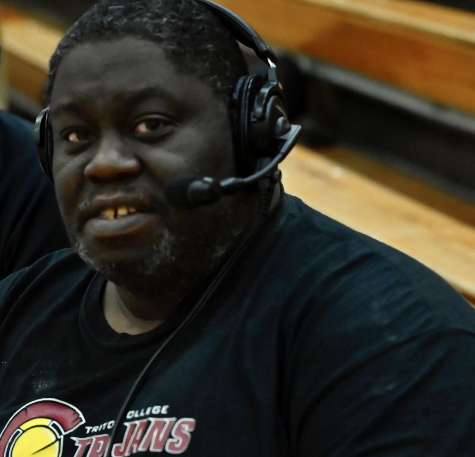A man wearing a headset sitting on a sports bench in a gymnasium.