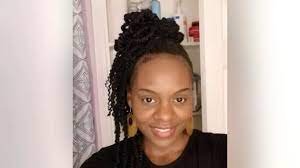 A woman with dark braided hair styled in an updo, smiling in front of a white door.