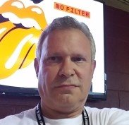 A man taking a selfie in front of a screen displaying a cartoon character and the words "NO FILTER".