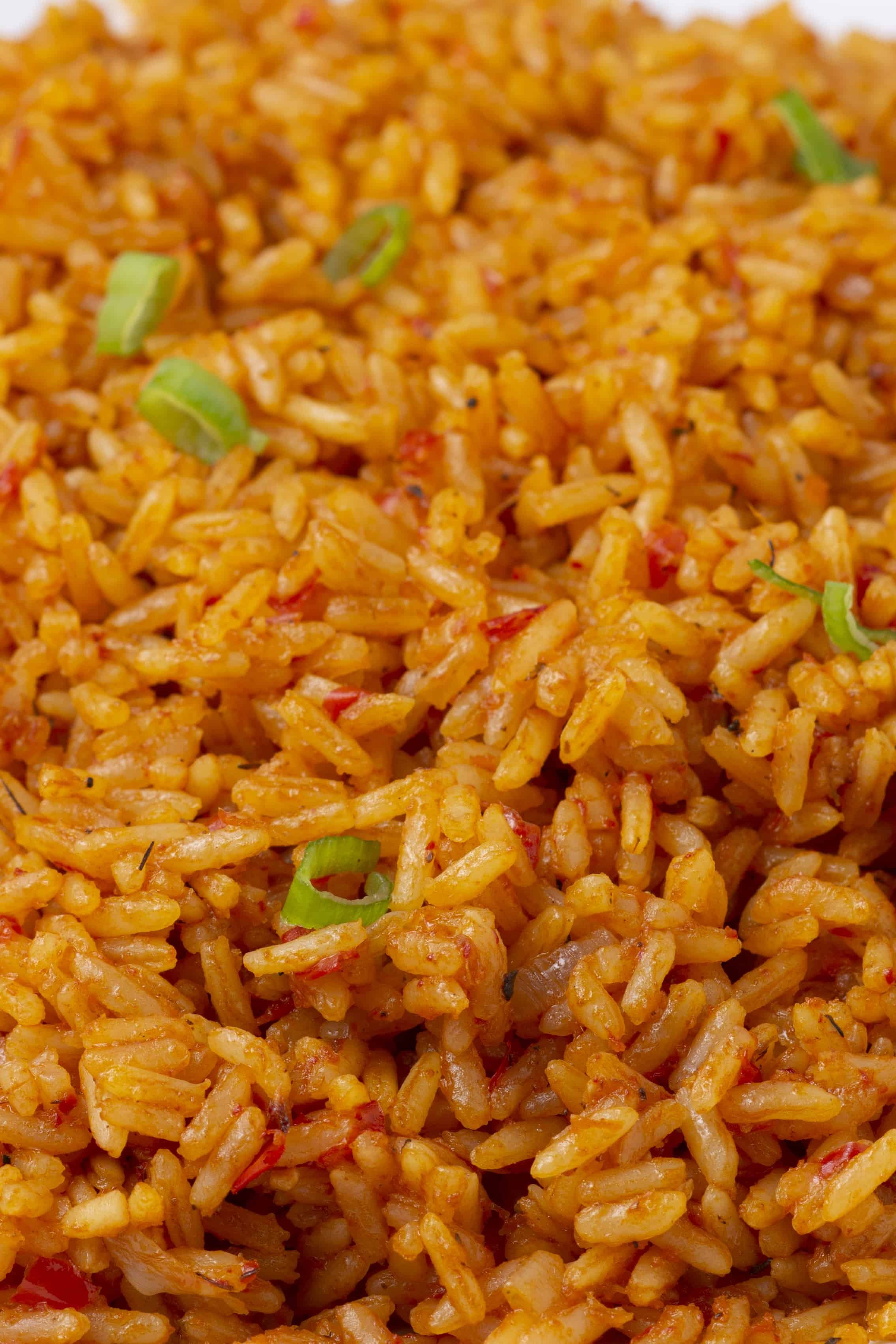 Close-up of cooked fried rice with small pieces of red pepper and sliced green onions.