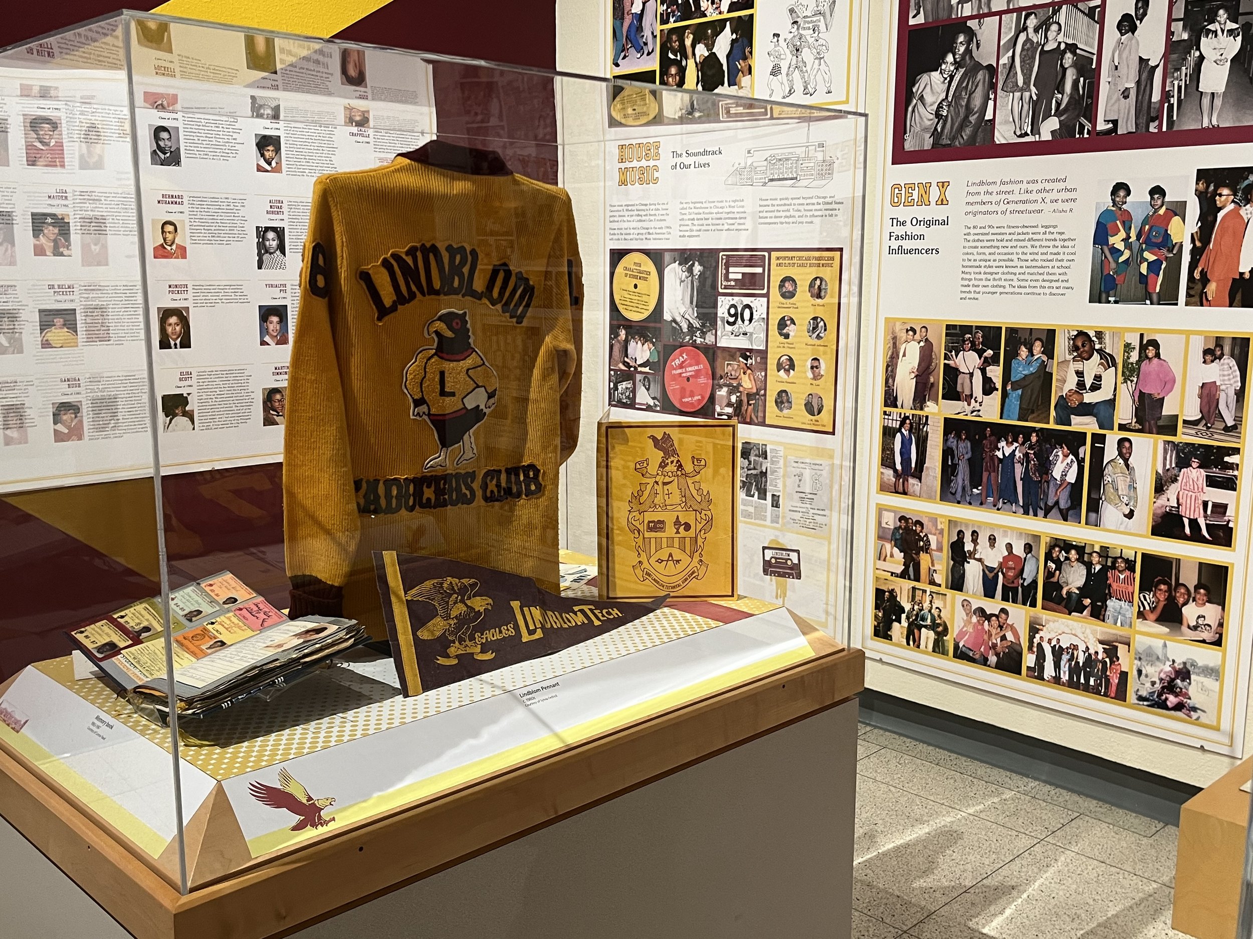 Museum display featuring a yellow Football club jacket with 'LINDBlOM' logo, historical photos on the wall, and informational panels about fashion influences and the history of Lindblom fashion.