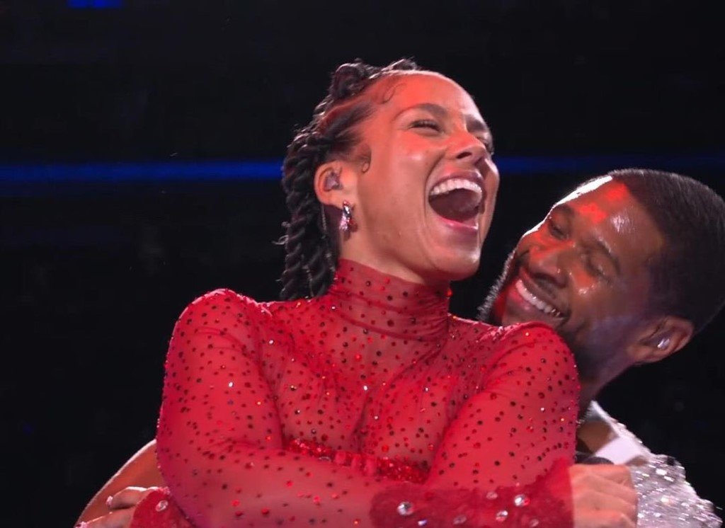 Two people, a woman in a red dress and a man, are joyfully hugging and smiling.